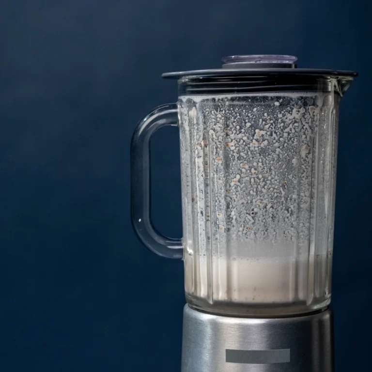 Blended protein shake in a glass beside a blender