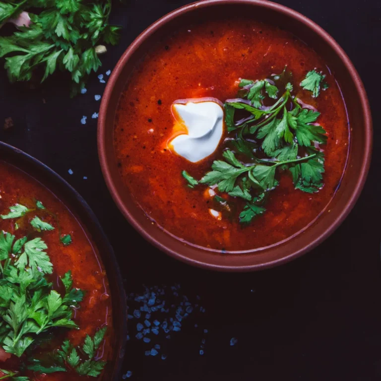 A white bowl of creamy ground beef and tomato soup topped with chopped parsley