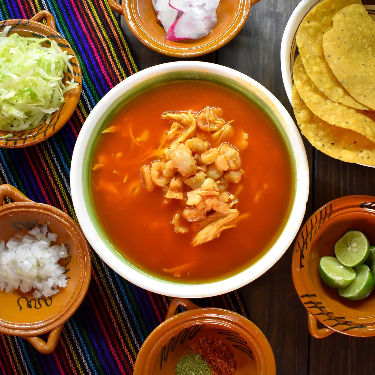 A bowl of red chicken tortilla soup topped with crisp tortilla strips, avocado and cilantro