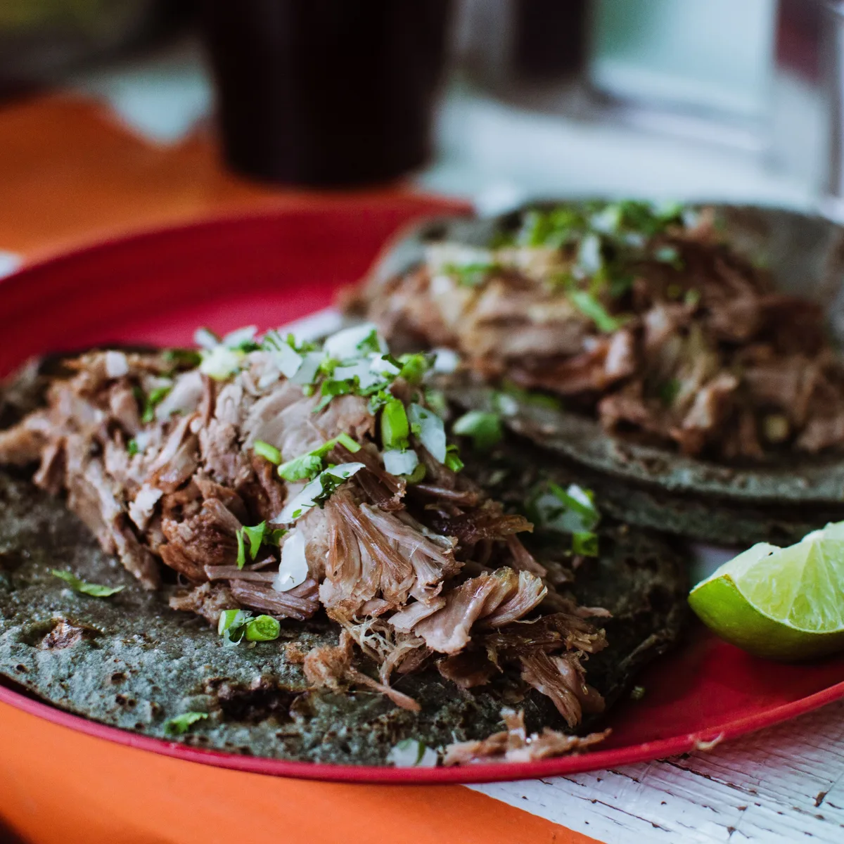 Barbacoa tacos of shredded braised meat on blue corn tortillas with onion, cilantro and lime
