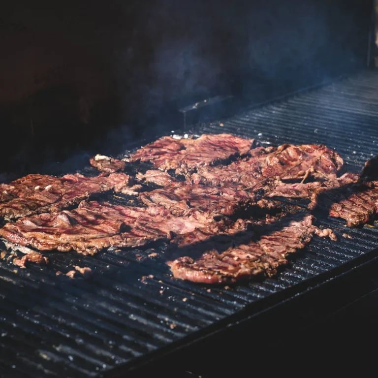 Thin cuts of marinated carne asada searing over a hot grill grate