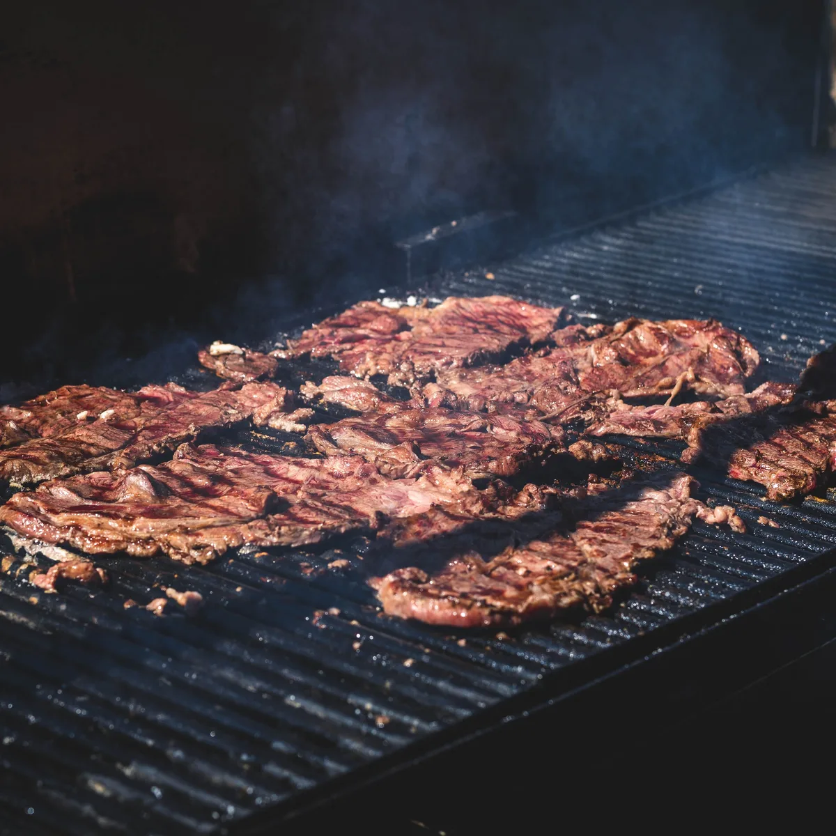 Thin cuts of marinated carne asada searing over a hot grill grate