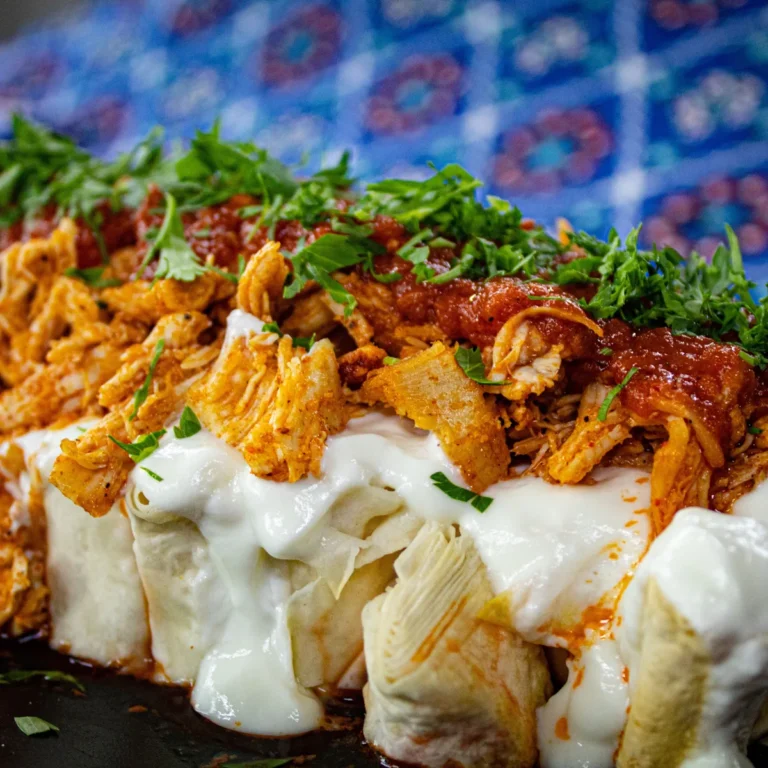 Rolled enchiladas topped with melted cheese, red sauce and shredded chicken