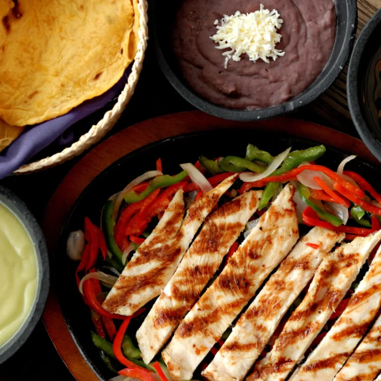 Grilled chicken fajitas over peppers and onions in a cast iron skillet with tortillas, guacamole and beans