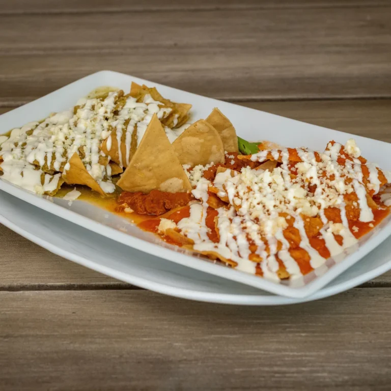 A plate of chilaquiles, half in green salsa and half in red, with crema and crumbled cheese