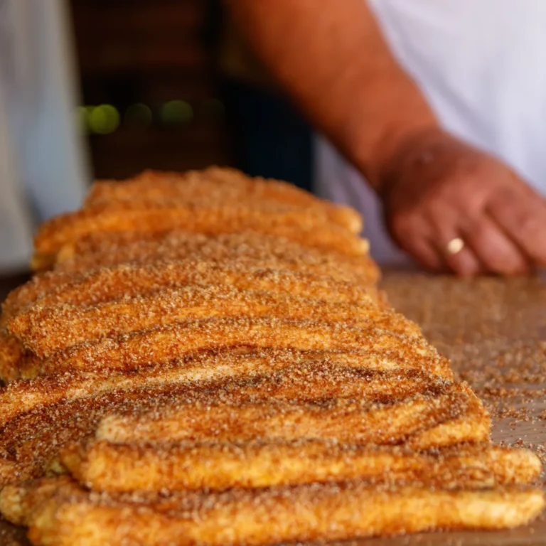Freshly fried ridged churros dusted with cinnamon sugar on a wooden counter