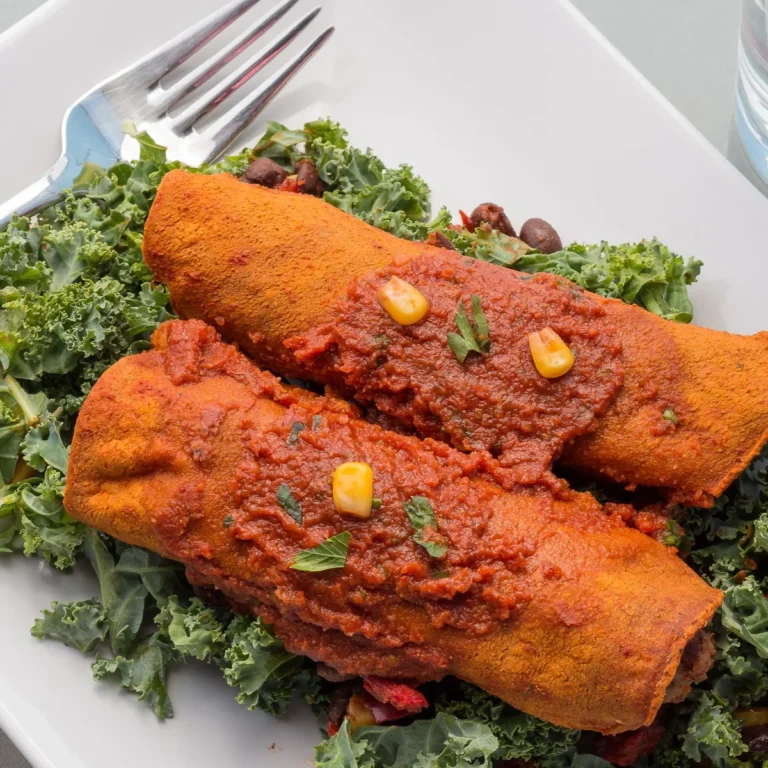 Two enchiladas smothered in red chile enchilada sauce on a bed of kale