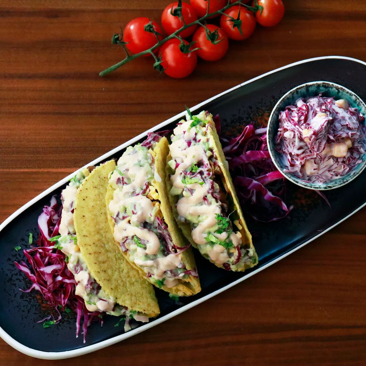 Crisp-shell tacos of flaked white fish with creamy sauce, beside a bowl of red cabbage slaw