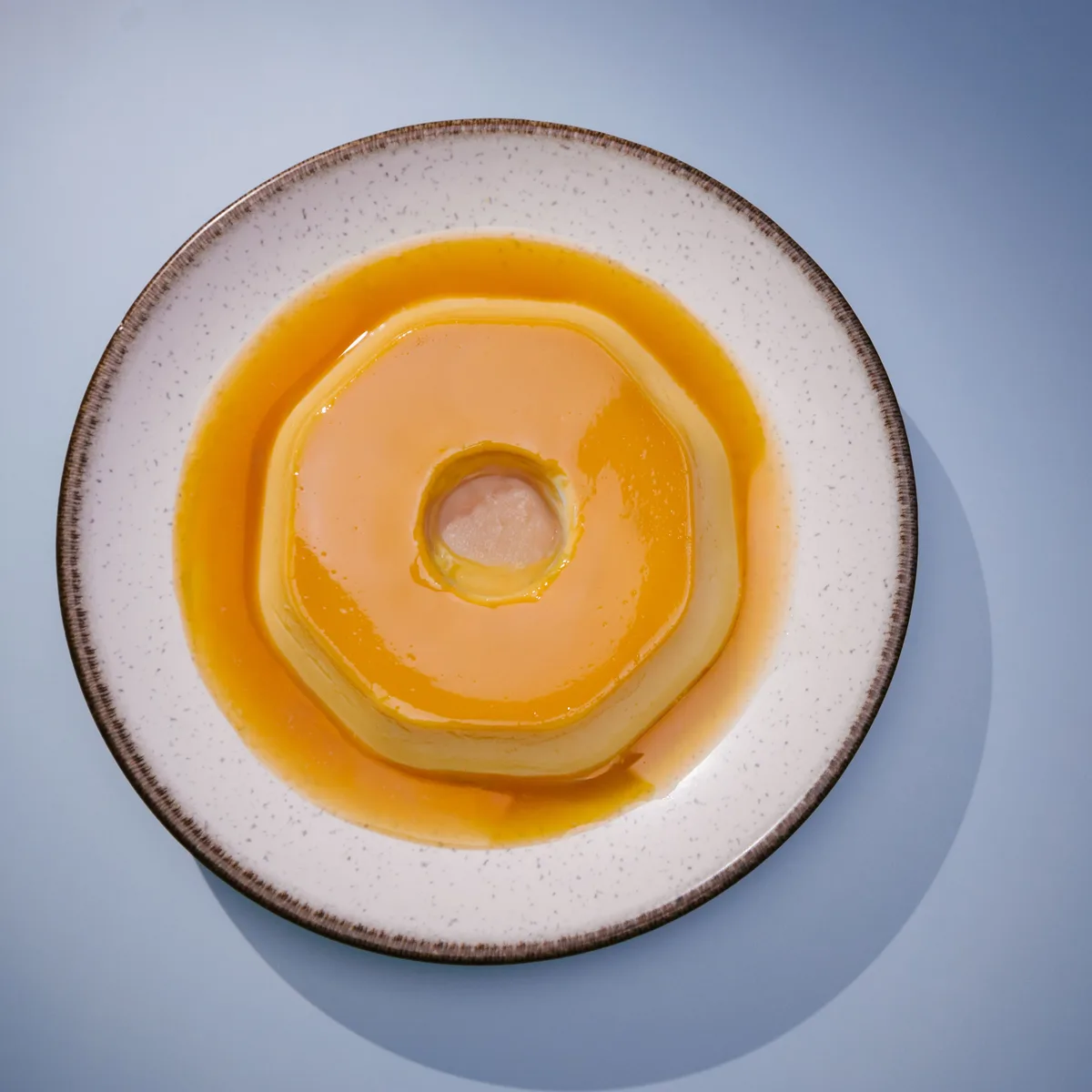 A whole flan turned out onto a white plate with caramel pooling around it