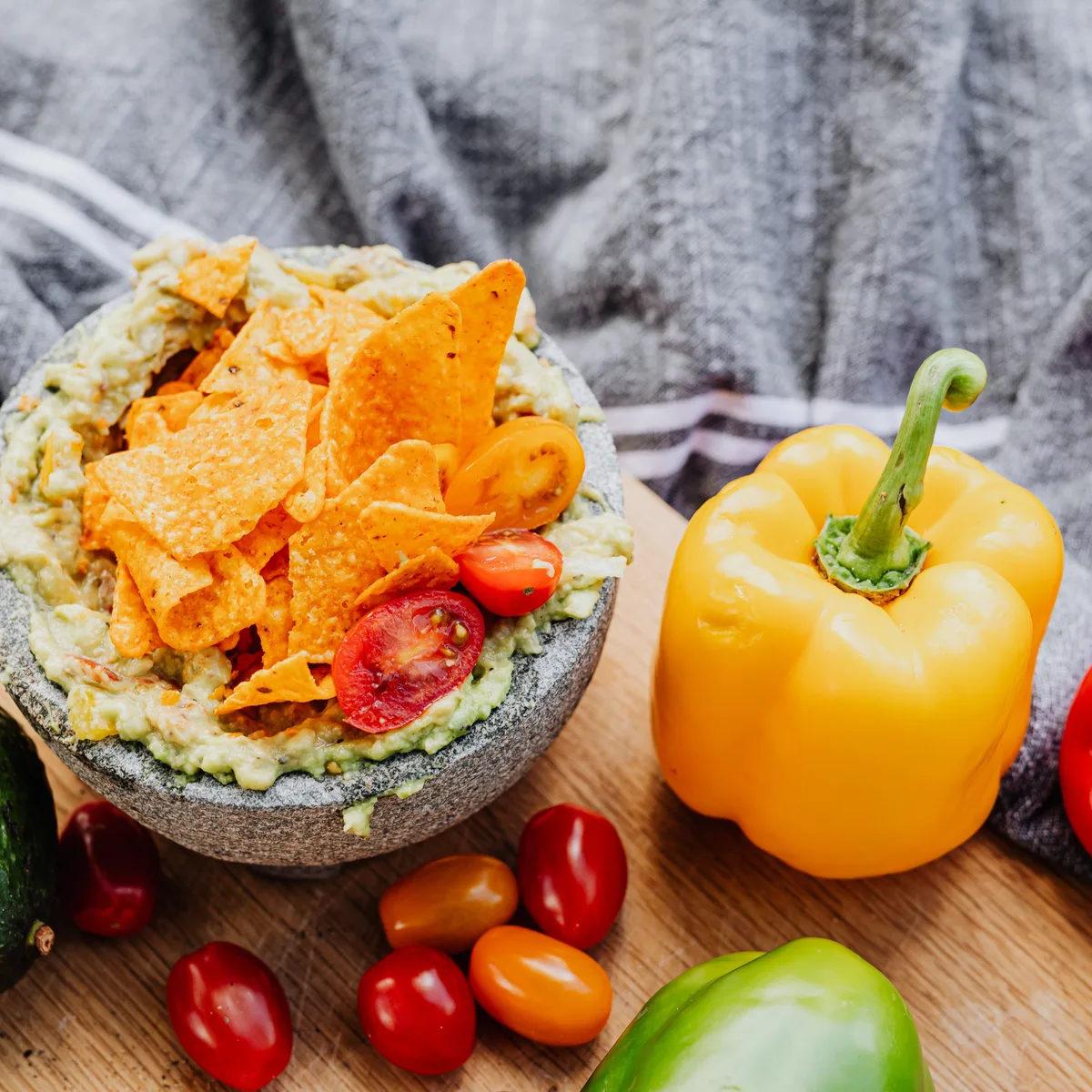 Chunky guacamole in a stone molcajete topped with tortilla chips and halved cherry tomatoes