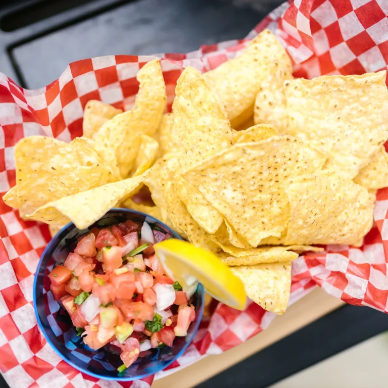 A small bowl of fresh pico de gallo with a lime wedge beside a basket of tortilla chips
