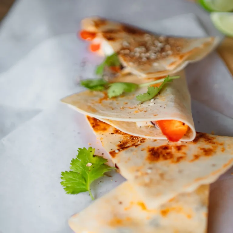 Quesadilla wedges on wax paper with cilantro and lime alongside