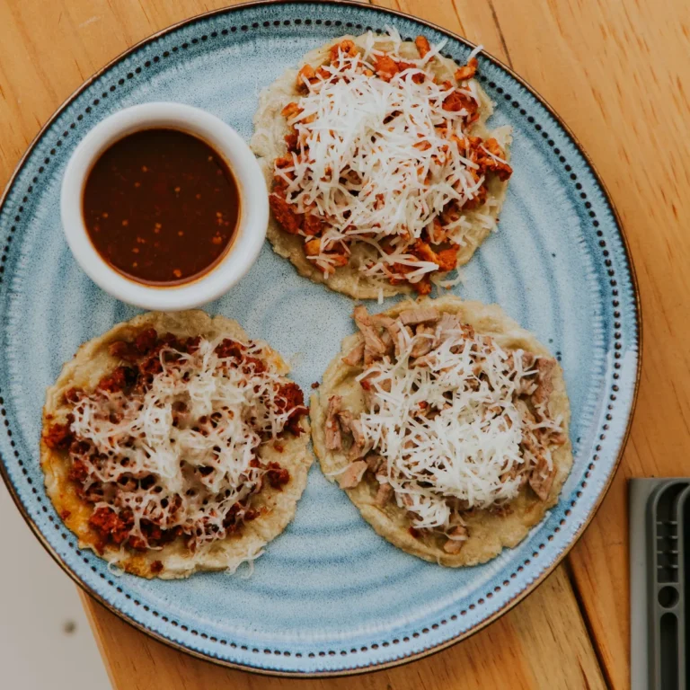 Three thick masa sopes topped with red sauce and crumbled cheese, with salsa alongside