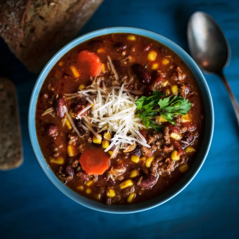 A bowl of beef and bean soup with corn, topped with shredded cheese and herbs