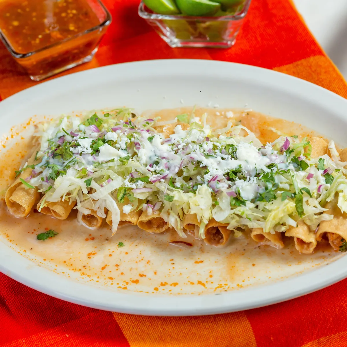 A plate of crisp rolled taquitos with shredded lettuce, crema and salsa