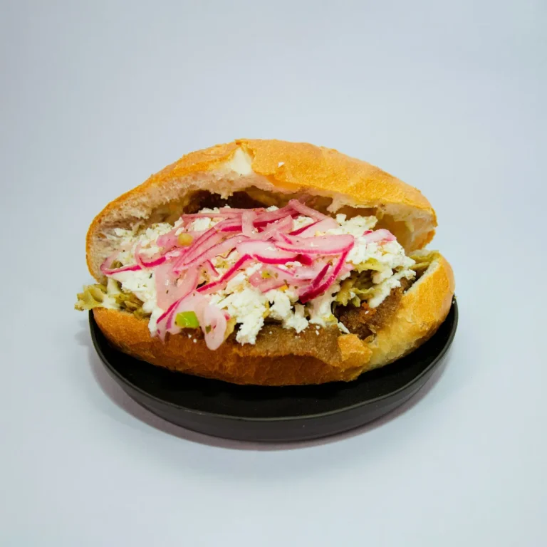 An open Mexican torta on a crusty roll, topped with shredded filling, pickled onions and cheese