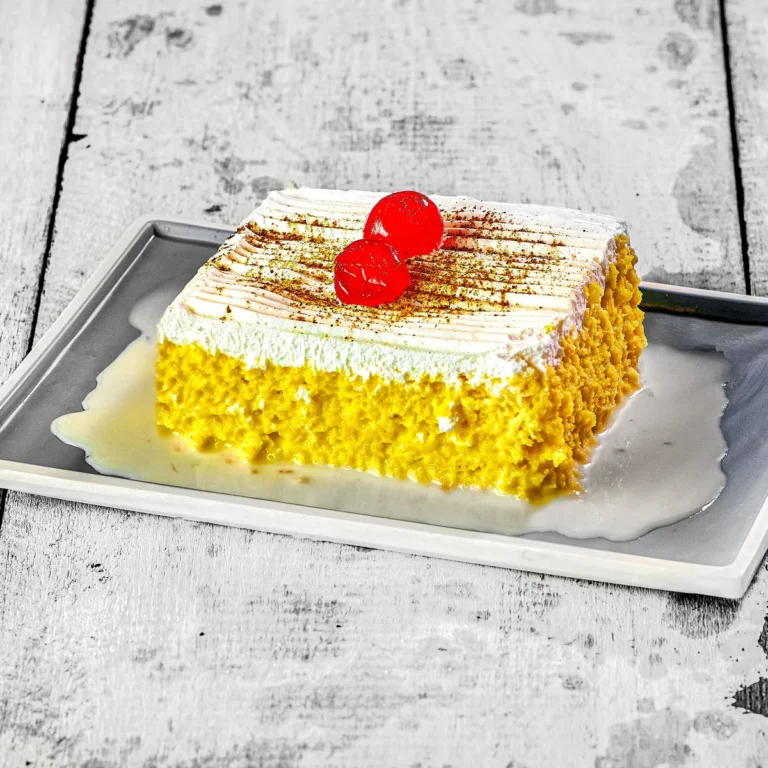 A slice of tres leches cake topped with whipped cream and cherries