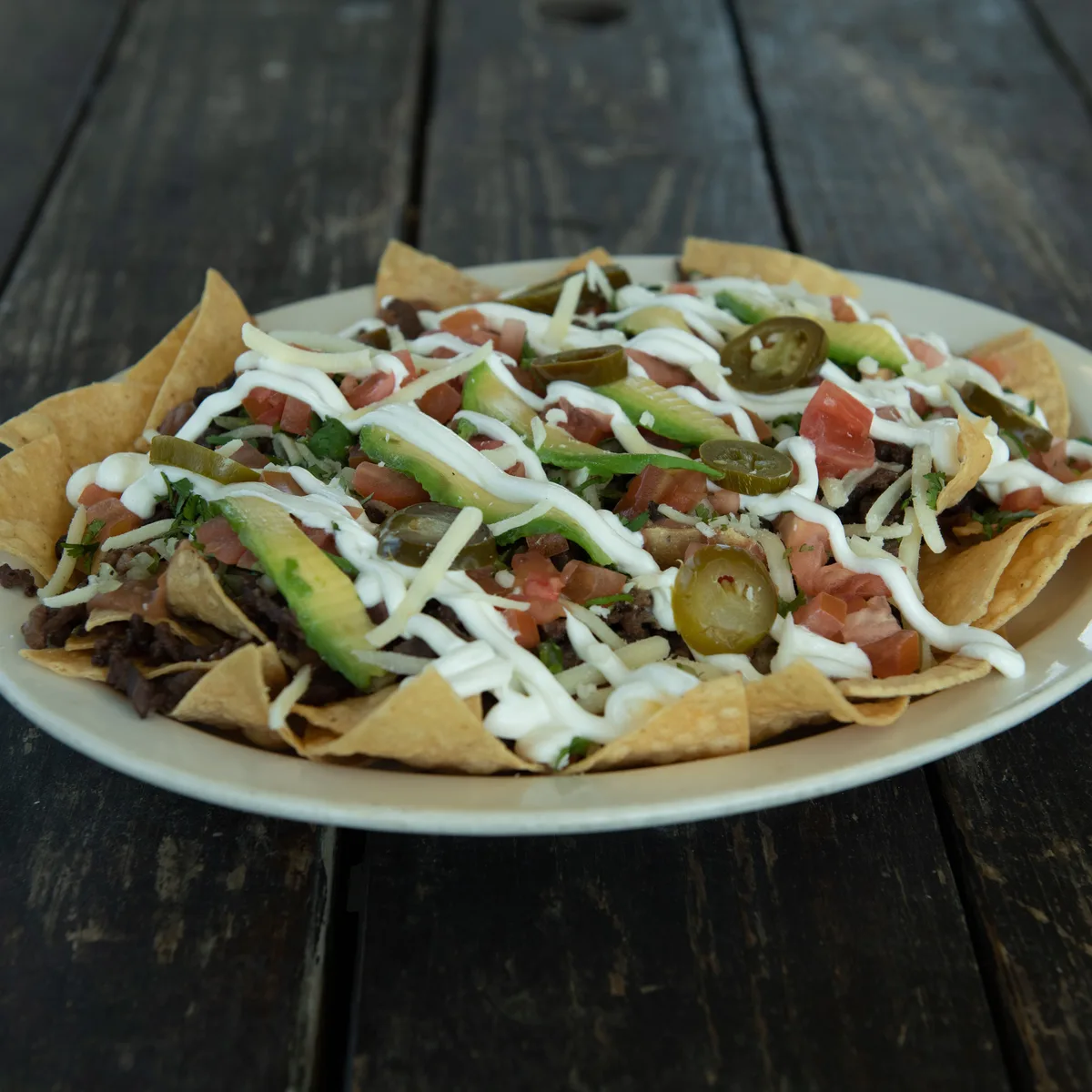 A plate of beef nachos with melted cheese, jalapenos, guacamole and sour cream
