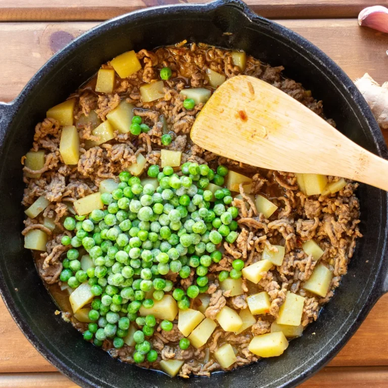 A skillet of ground beef with diced potato and peas
